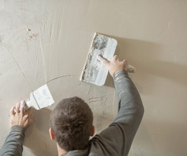 a man stands at a rough plastered wall with spatulas.